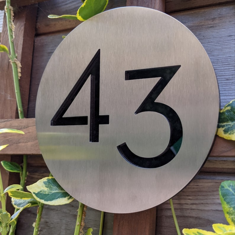 May include: A round, silver metal house number sign with the number 43 in black.