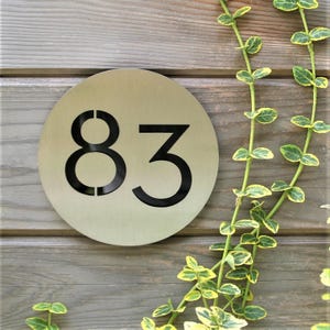 May include: A round, silver-colored metal house number sign with the number 83 cut out in black.