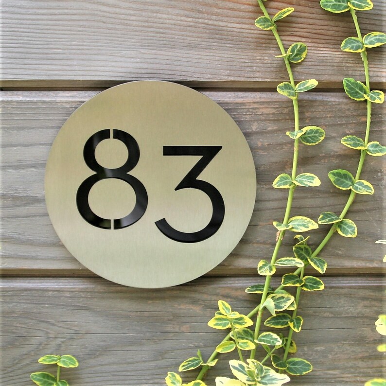 May include: A round, silver-colored metal house number sign with the number 83 cut out in black.