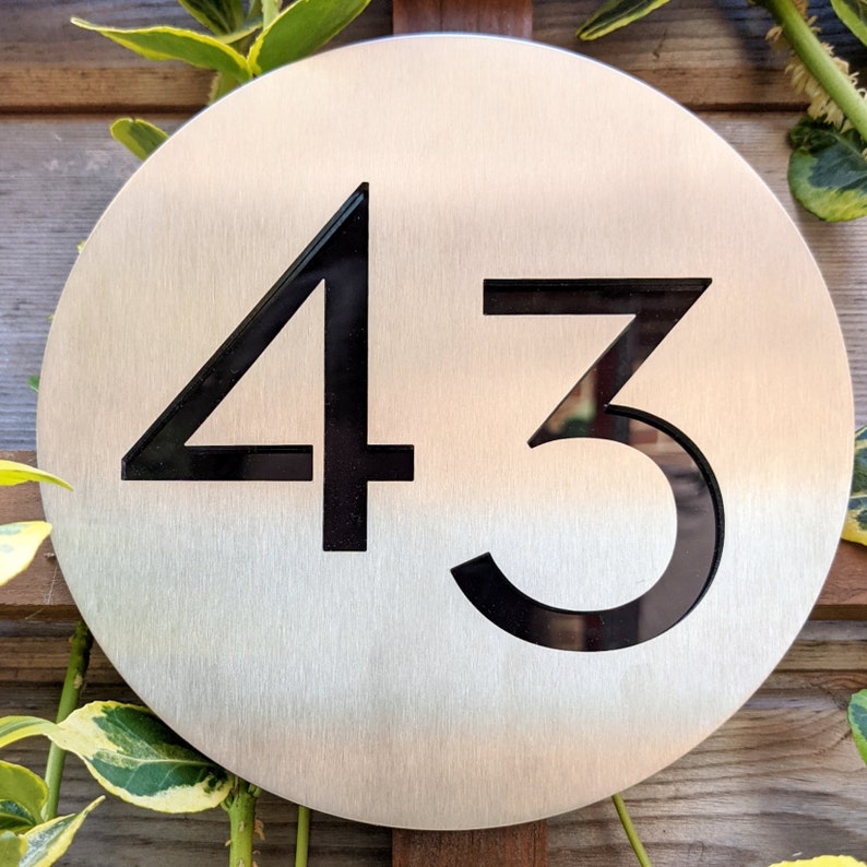 May include: A round, silver-colored metal sign with the number 43 printed in black.