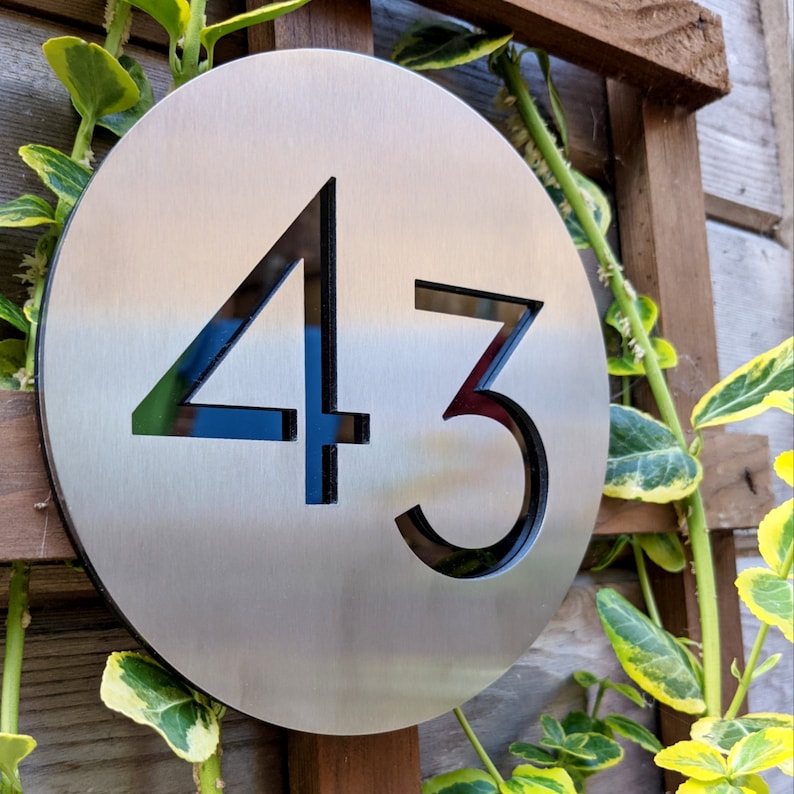 May include: A round, silver metal house number sign with the number 43 cut out in black.