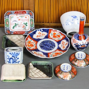 May include: A collection of vintage Japanese porcelain dishes and a vase. The dishes are decorated with intricate floral patterns in shades of blue, red, and gold. The vase is a tall, slender shape with a bulbous base and a narrow neck. It is decorated with a floral pattern in shades of blue, red, and white.