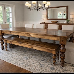 May include: A large, rectangular wooden dining table with a matching bench and chairs. The table and bench are a warm brown color, and the chairs have cream-colored slipcovers. The room has a rug with a floral pattern.