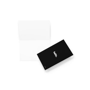May include: A white, blank greeting card is open, next to a closed black card. The black card has the word "hello." in white, sans-serif font. The cards are on a white background.