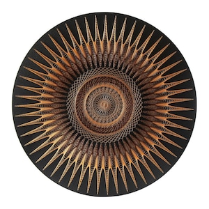 May include: A circular wall hanging with a black background and a gold and brown geometric design. The design is made up of concentric circles and radiating lines.