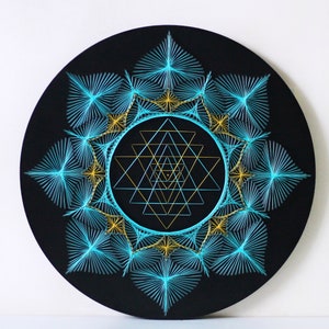 May include: A circular wall hanging with a black background and a geometric design in turquoise and gold thread. The design features a Sri Yantra, a sacred symbol in Hinduism, surrounded by a mandala-like pattern.