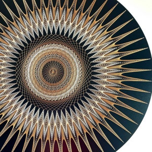 May include: A black circular wall art piece with a gold and white geometric design. The design features a central circle with radiating lines and a starburst pattern.