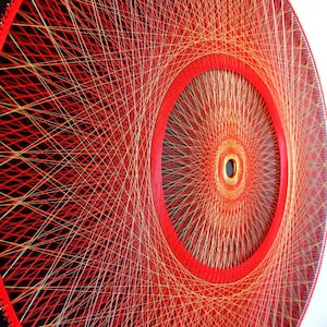 May include: A circular wall hanging made of string art. The string is red and gold, creating a radial pattern with a central circle. The background is black.