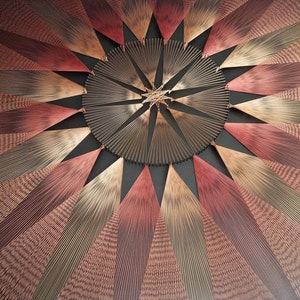 May include: A circular wall hanging made of string in shades of red, brown, and gold. The strings are arranged in a radial pattern, creating a starburst effect.