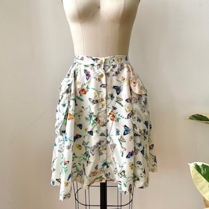 May include: A white skirt with a butterfly print. The skirt has a button closure and two pockets on the sides. The skirt is on a white mannequin.