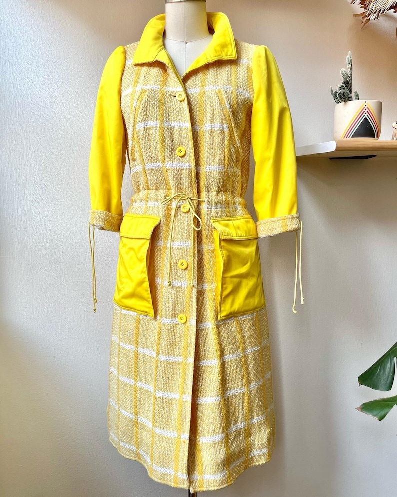 May include: A yellow and white plaid dress with a yellow long-sleeved jacket. The dress has a drawstring waist and two large pockets.