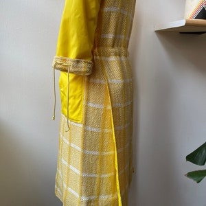 May include: A yellow and white checkered coat with a yellow lining. The coat has a drawstring waist and a long, flowing silhouette.
