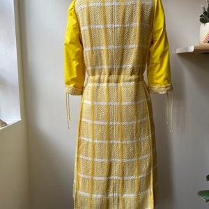 May include: A yellow and white plaid dress with a cinched waist and yellow sleeves. The dress is on a mannequin.