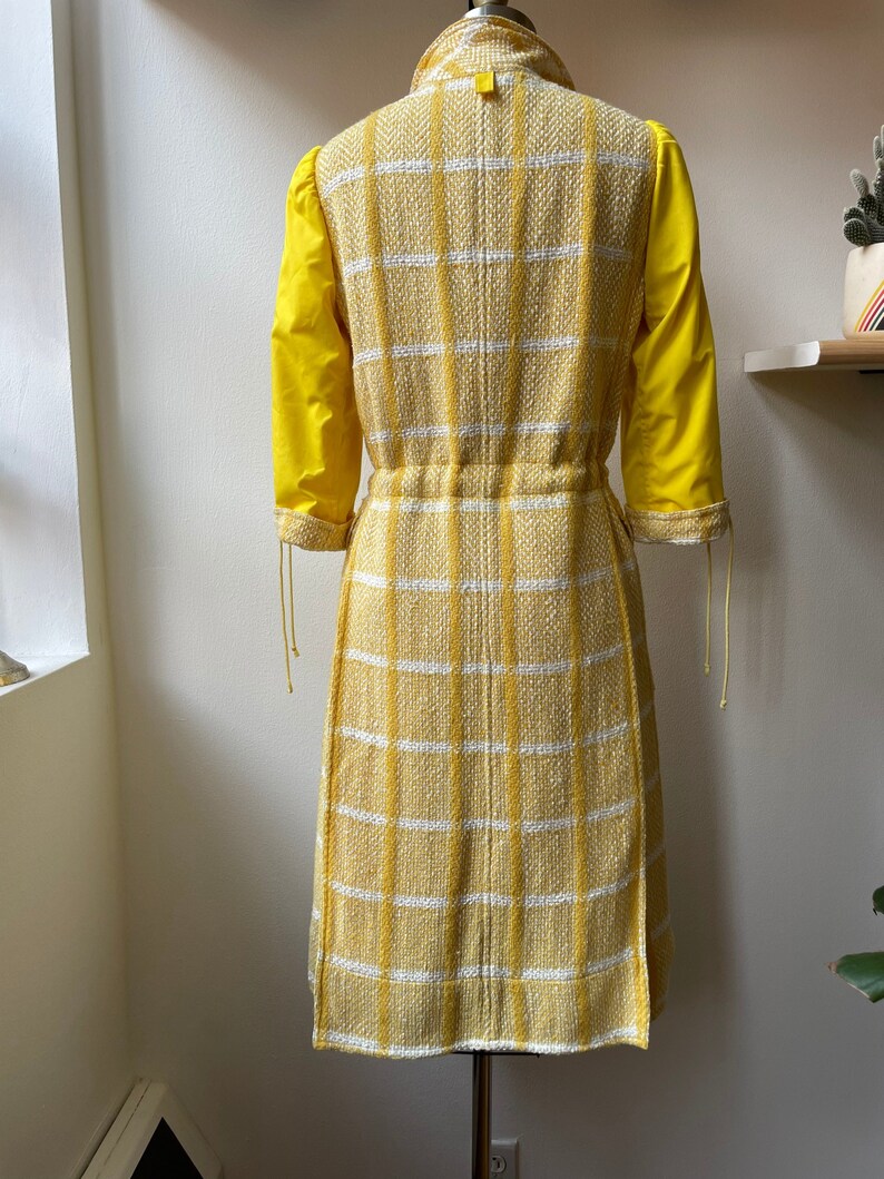 May include: A yellow and white plaid dress with a cinched waist and yellow sleeves. The dress is on a mannequin.