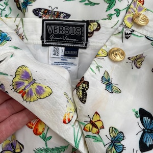 May include: White button-up shirt with a butterfly print. The shirt has a label that reads "VERSUS Gianni Versace" and size information: "28 1 42".