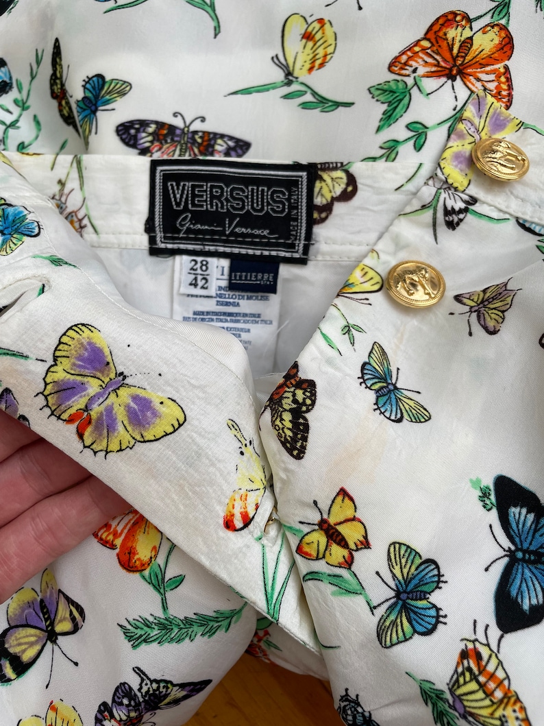 May include: White button-up shirt with a butterfly print. The shirt has a label that reads "VERSUS Gianni Versace" and size information: "28 1 42".