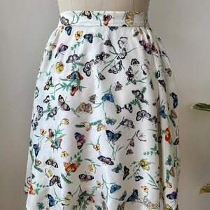 May include: A white skirt with a butterfly print. The butterflies are in various colors, including blue, yellow, orange, and green. The skirt is a-line and has a gathered waist.