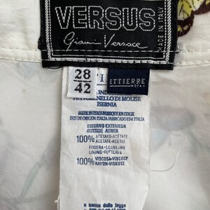 May include: White shirt with a butterfly print and a black label that says "VERSUS Gianni Versace" and "Made in Italy". The label also includes size information: 28 and 42. The fabric content is listed as 100% acetate and 100% rayon.