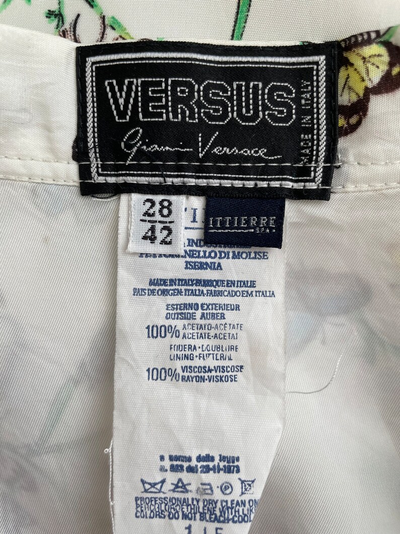 May include: White shirt with a butterfly print and a black label that says "VERSUS Gianni Versace" and "Made in Italy". The label also includes size information: 28 and 42. The fabric content is listed as 100% acetate and 100% rayon.