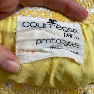 May include: A yellow and white tweed jacket with a white label that reads "Courreges Paris prototypes made in France".