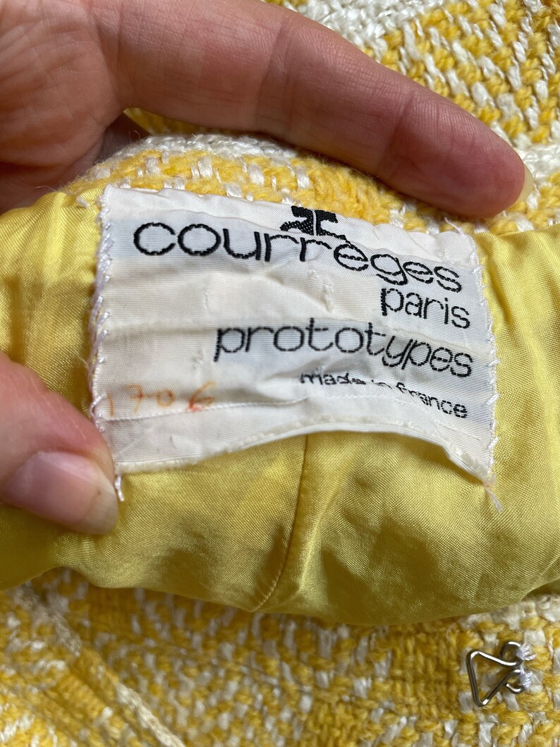 May include: A yellow and white tweed jacket with a white label that reads "Courreges Paris prototypes made in France".