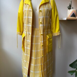 May include: A yellow checkered skirt and matching jacket with yellow solid sleeves. The jacket has a button closure and pockets.