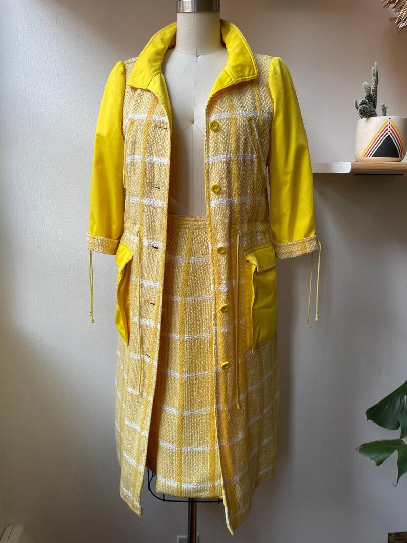 May include: A yellow checkered skirt and matching jacket with yellow solid sleeves. The jacket has a button closure and pockets.