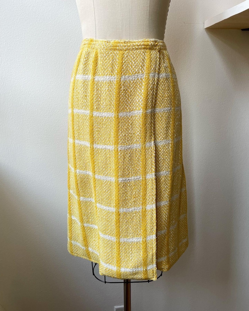 May include: A yellow and white plaid skirt with a wrap style design. The skirt is knee-length and has a straight silhouette.