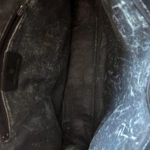 May include: Interior view of a black leather handbag. The bag's interior shows a zippered pocket and a leather tag with the Gucci logo. The leather has a distressed appearance with white markings throughout.
