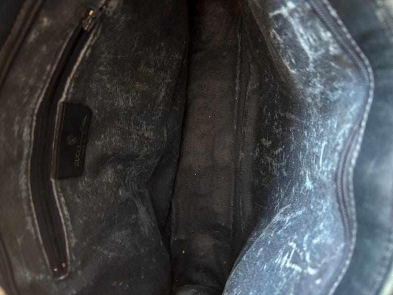 May include: Interior view of a black leather handbag. The bag's interior shows a zippered pocket and a leather tag with the Gucci logo. The leather has a distressed appearance with white markings throughout.