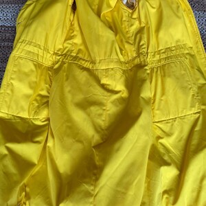 May include: A yellow raincoat with a white and yellow plaid trim. The raincoat has a hood and is unzipped, showing the yellow lining.