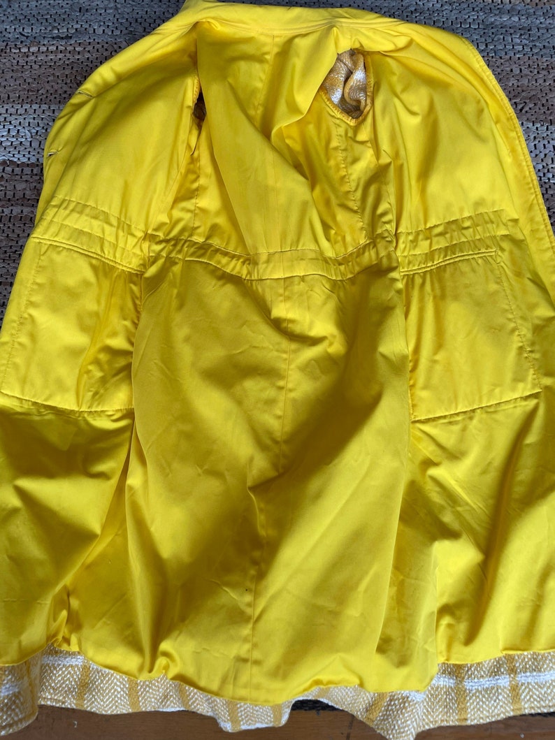 May include: A yellow raincoat with a white and yellow plaid trim. The raincoat has a hood and is unzipped, showing the yellow lining.