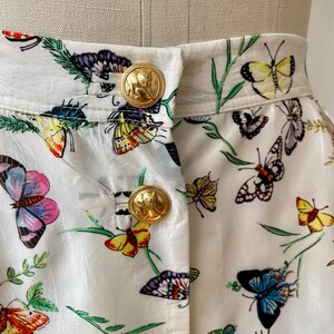 May include: White skirt with a butterfly print and gold buttons. The skirt has a high waist and a full skirt.