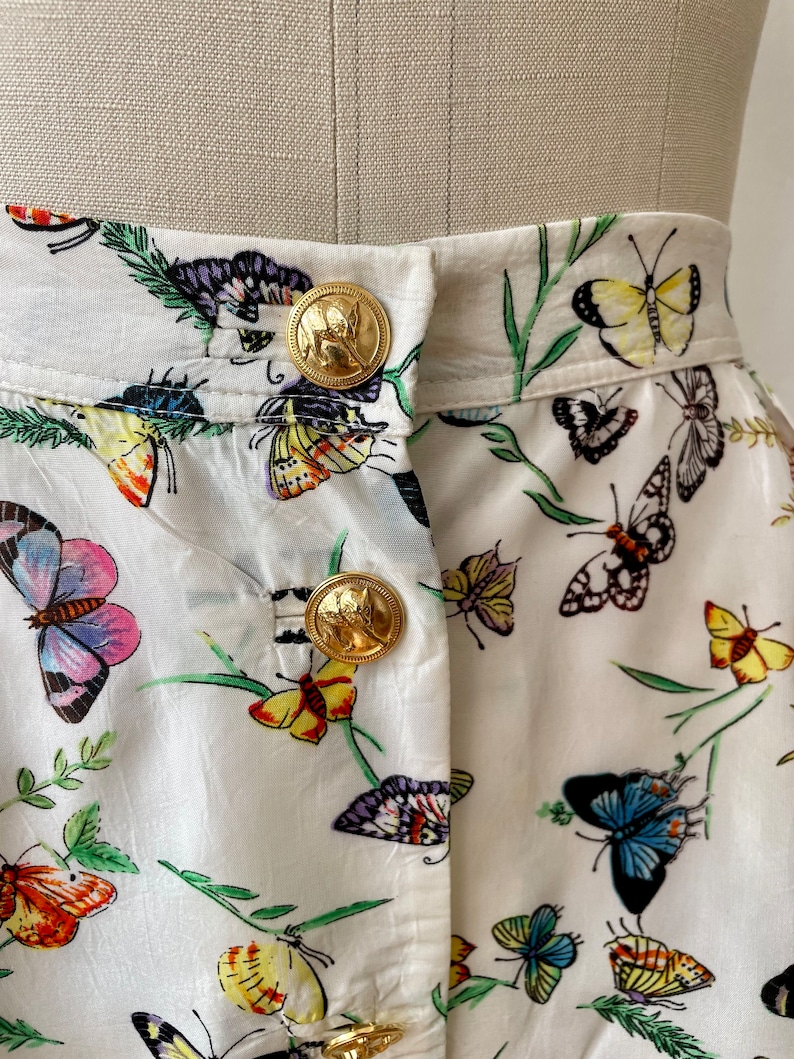 May include: White skirt with a butterfly print and gold buttons. The skirt has a high waist and a full skirt.