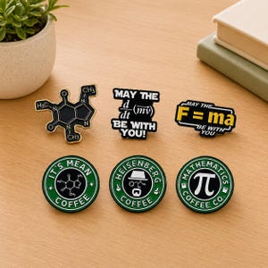 May include: A collection of enamel pins with science and math themes. Designs include a caffeine molecule, equations, and coffee-themed logos. The pins are black, white, and green, with text such as "May the Force be with you!" and "It's Mean Coffee."