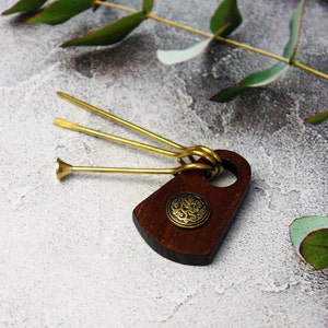 May include: A wooden pipe tool with a dark brown finish, featuring a brass emblem and three brass tools. The tool has a rounded shape with a hole and a decorative brass button. The brass tools include a poker, a tamper, and a reamer.