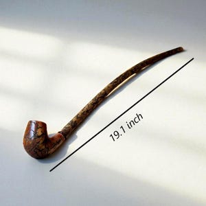 Peut inclure: Une pipe en bois, d'environ 48,5 cm de long, avec un tuyau incurvé et un foyer. La pipe présente un motif texturé distinctif en marron et beige. Conçue pour fumer.