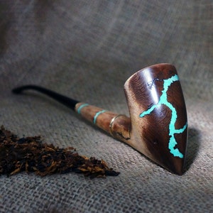 Puede incluir: Una pipa de fumar de madera con un acabado marrón oscuro y detalles turquesa. La pipa tiene una cazoleta curva y una boquilla larga y fina.