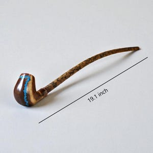 May include: A long, curved wooden smoking pipe featuring a polished brown bowl with a textured turquoise inlay and a mottled, dark-patterned stem. The pipe is shown with a line indicating a total length of 48.5 cm for the entire object.