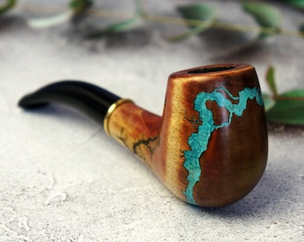 May include: A wooden smoking pipe with a black stem and a brown bowl. The bowl is decorated with a turquoise blue resin design.