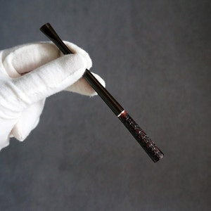 以下が含まれることがあります： テクスチャ加工されたデザインの黒と赤のタバコホルダー