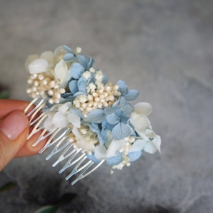 May include: A silver hair comb decorated with dried blue and white flowers. The comb is 3.15 inches long.