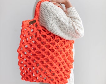 May include: Bright orange crocheted tote bag with a rectangular shape. The bag has a large open weave design and a brown leather tag. The bag is carried over the shoulder. The bag is made of a thick, durable yarn.