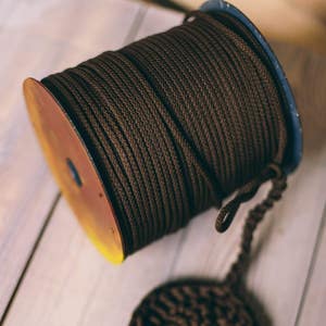 May include: A spool of brown rope with a blue and yellow rim, and a matching circular piece of rope. The rope is tightly wound on the spool. The circular piece is made of the same brown rope.