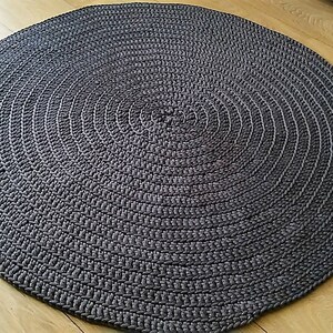 May include: A round, gray, crocheted rug with a circular pattern. The rug is made of thick, textured yarn and has a slightly raised surface.