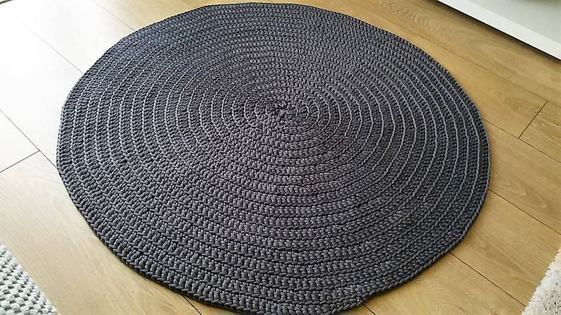 May include: A round, gray, crocheted rug with a circular pattern. The rug is made of thick, textured yarn and has a slightly raised surface.