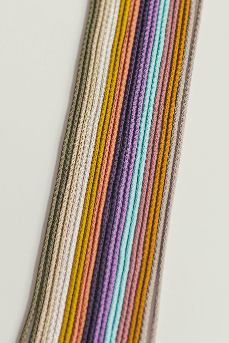May include: A collection of colorful cords in various shades, including beige, yellow, orange, purple, and blue. The cords are arranged diagonally against a white background, showcasing their texture and color variations. Ideal for crafting or decorative purposes.
