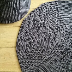 May include: A gray round crocheted rug with a circular pattern. The rug is made of thick yarn and has a textured surface.