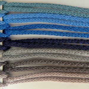 May include: A color chart displaying braided cords in various shades of blue, gray, and brown. The cords are labeled with numbers from 201 to 207, showcasing a range of hues from light blue to dark gray. The texture of the cords is clearly visible.