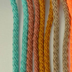 May include: A close-up of six braided cords in various colors: turquoise, coral, mustard yellow, tan, and bright orange. The cords are looped at the top and numbered 51 through 55. The cords are made of a soft, flexible material.